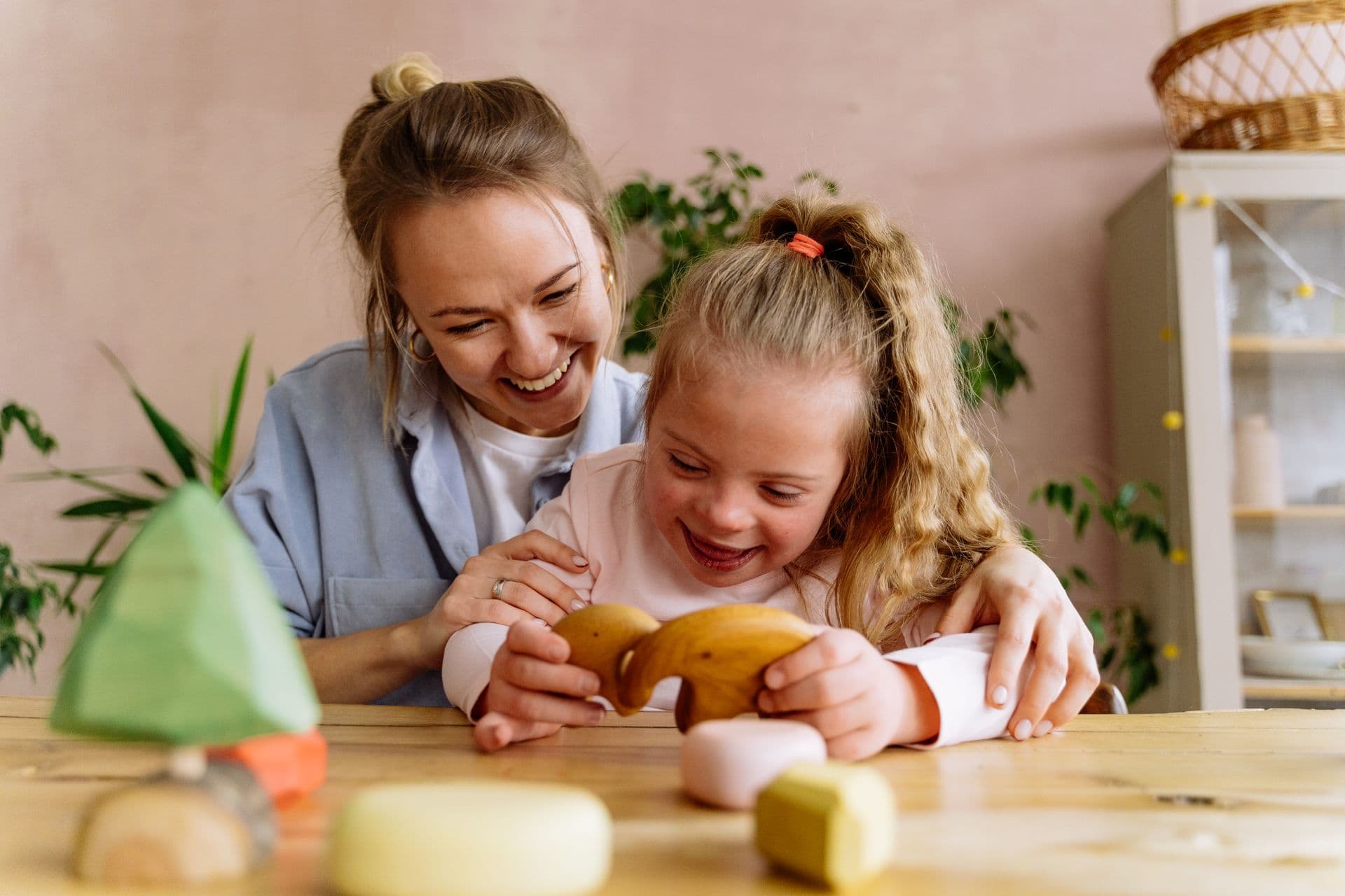 A mentor and child laughing together over wooden toys